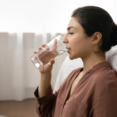 A person's mouth with a glass of water nearby, symbolizing the potential treatment for dry mouth