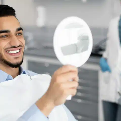 Happy handsome man looking at his teeth in a dental mirror after treatment