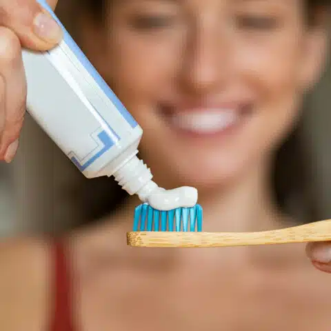Woman smiling while putting toothpaste on toothbrush