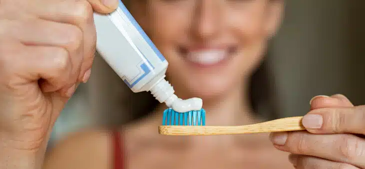 Woman smiling while putting toothpaste on toothbrush