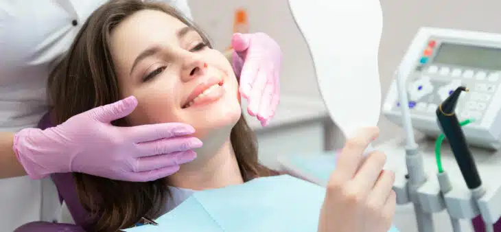 Woman sitting in dental chair looking at smile in mirror
