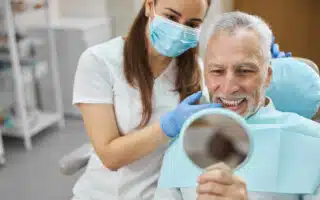 Older man looking at his teeth in a dental mirror with dentist