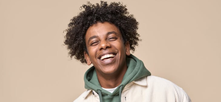 Man with perfect teeth smiling in front of a brown background